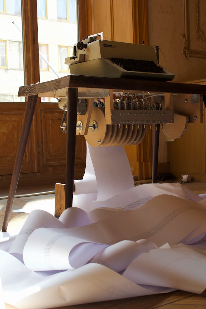 A retro typewriter on a wooden table with a long paper roll cascading to the floor, sunlight streaming through windows.
